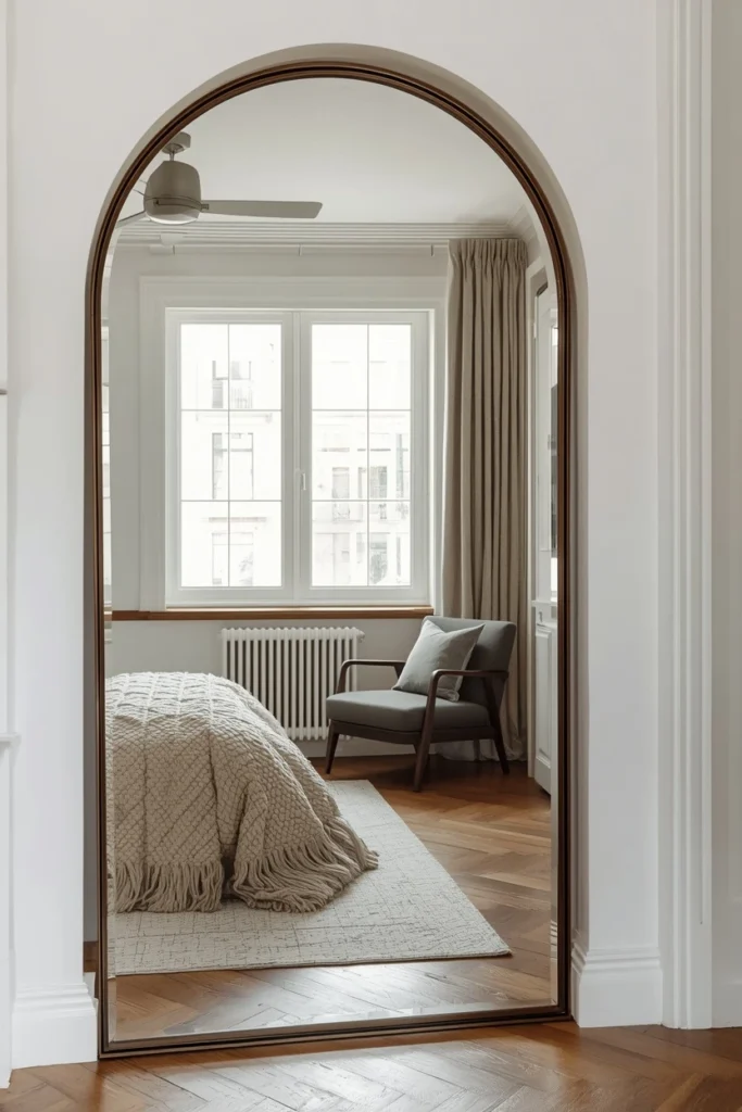 Arched mirror reflecting light in small bedroom